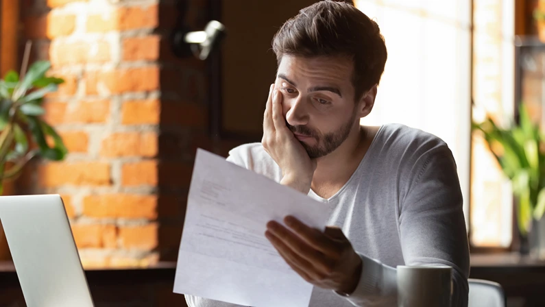 Confused frustrated young man reading letter in cafe