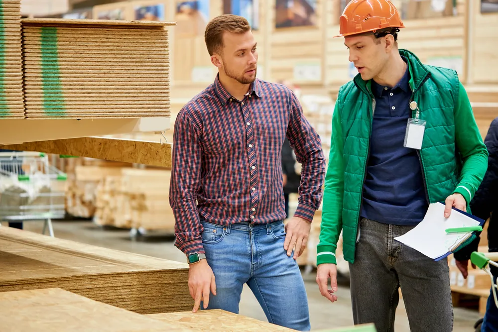 Two workers discussing wood materials in a warehouse, highlighting supply chain management and inventory control practices.