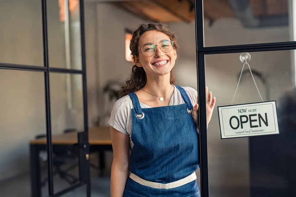 A small business owner proudly holding an 'OPEN' sign, symbolizing success from grant-funded economic development.