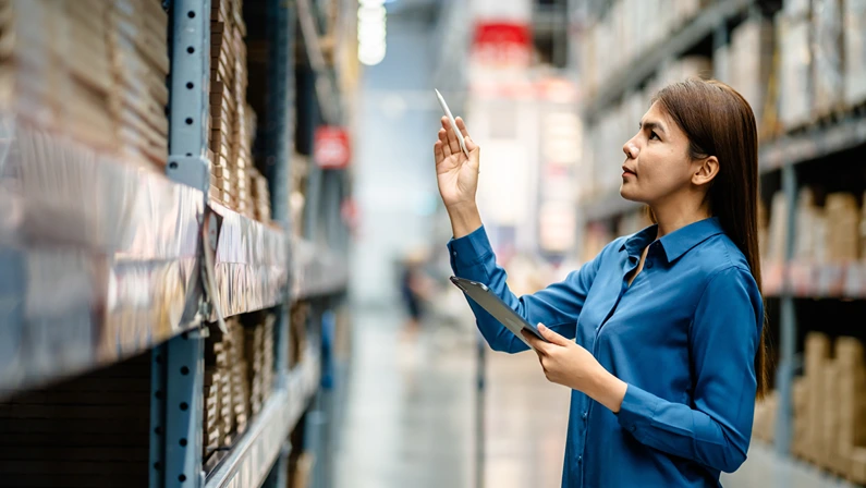 Warehouse worker inspecting inventory with a tablet, representing supply chain risk management and operational efficiency.