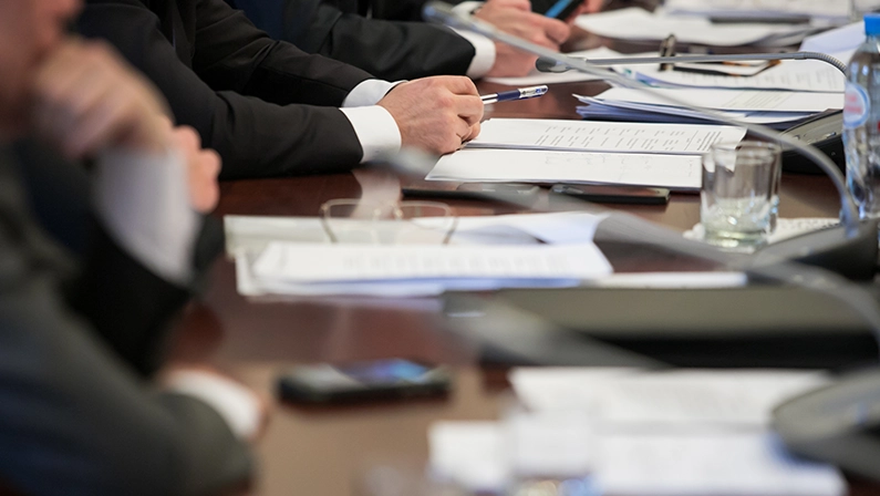 Government officials in a formal meeting reviewing documents, discussing policies and funding for infrastructure development.