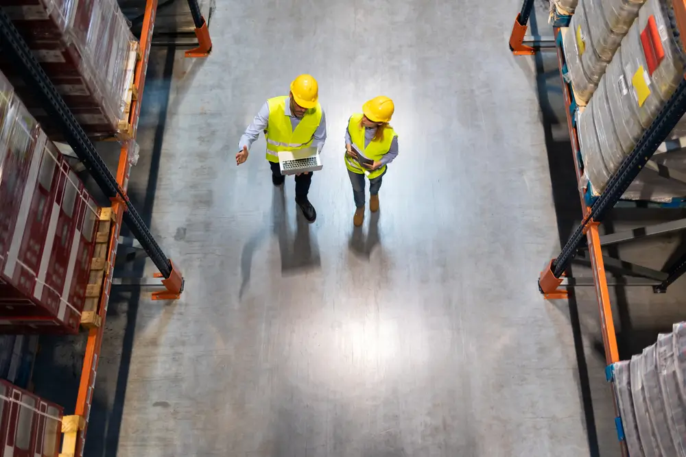 Warehouse managers consult plans using laptop, above view