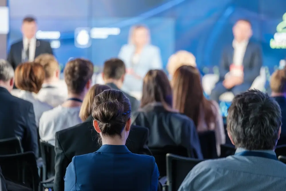 Rear view of a business audience listening to a speaker at a conference.