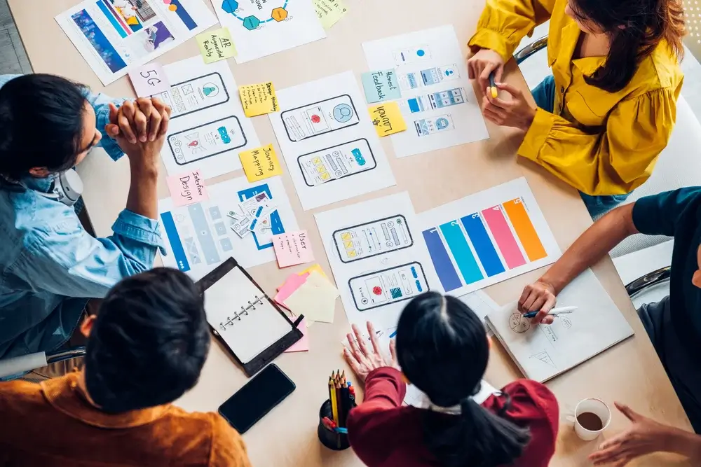 A creative group designing user interface concepts with sticky notes and charts, illustrating innovation in Small Business Innovation Research Assistance.