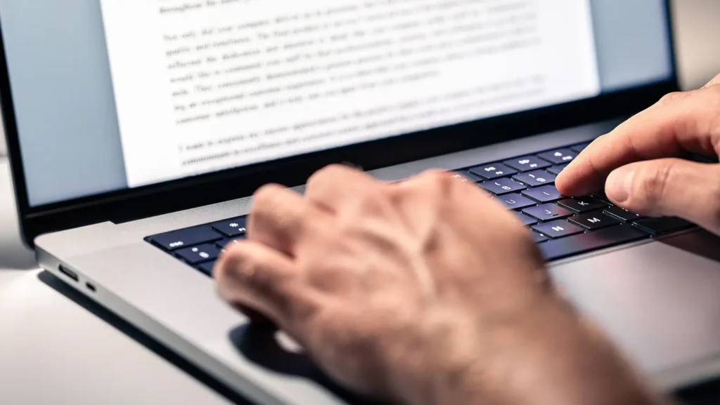 Close-up of hands typing on a laptop, writing a proposal after hiring a grant writer to secure funding for a project.