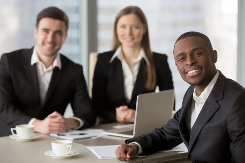 Attractive afro american cheerful businessman looking at camera sitting at desk young african manager leading meeting for subordinates at background business consulting multiracial team leadership