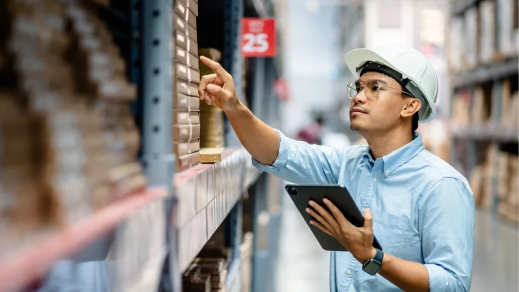 Warehouse worker checks inventory on shelves while using tablet, demonstrating effective inventory management strategies.