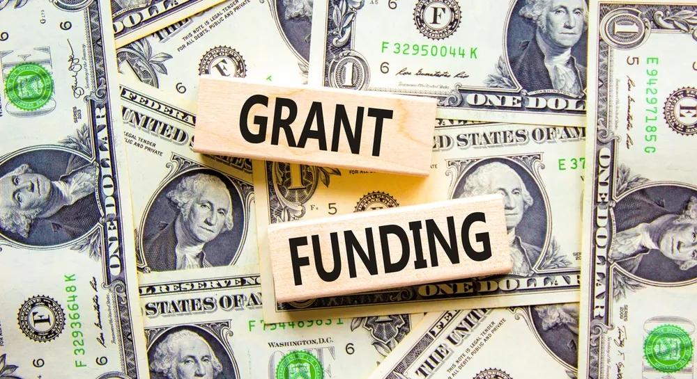 Wooden blocks reading 'GRANT' and 'FUNDING' placed on dollar bills, illustrating support from national and federal grants.