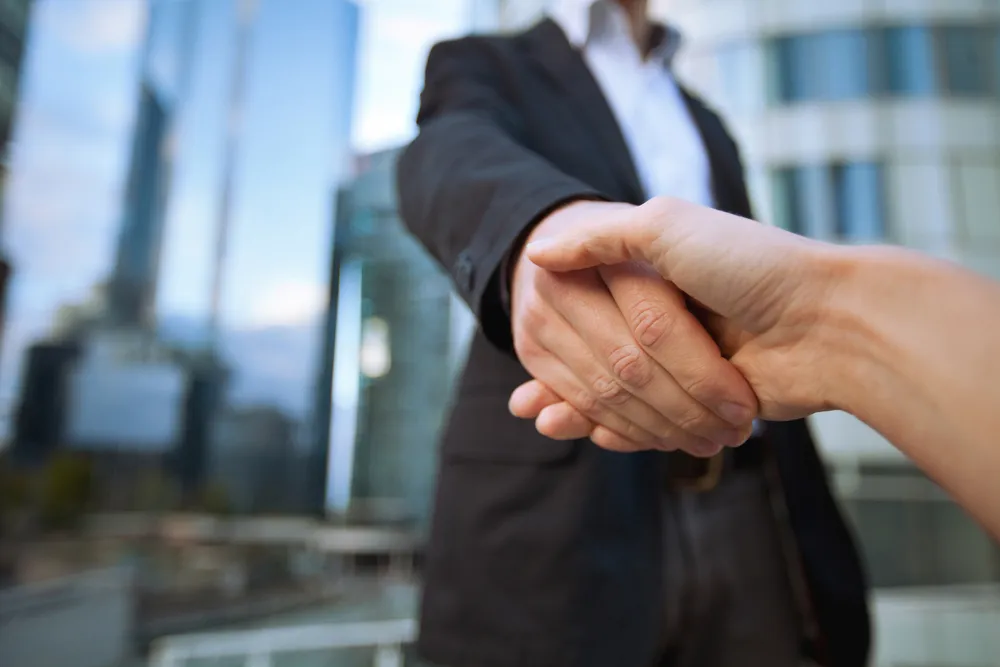 Two people shaking hands outside an office, symbolizing partnerships made possible by national and federal grants.