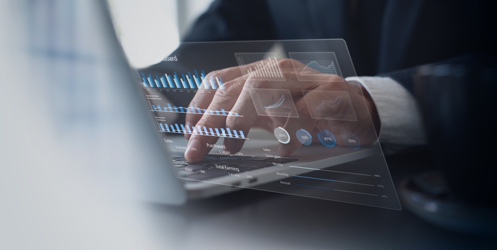 Hands typing on laptop keyboard with graphs and charts displaying real-time competitive intelligence data.=