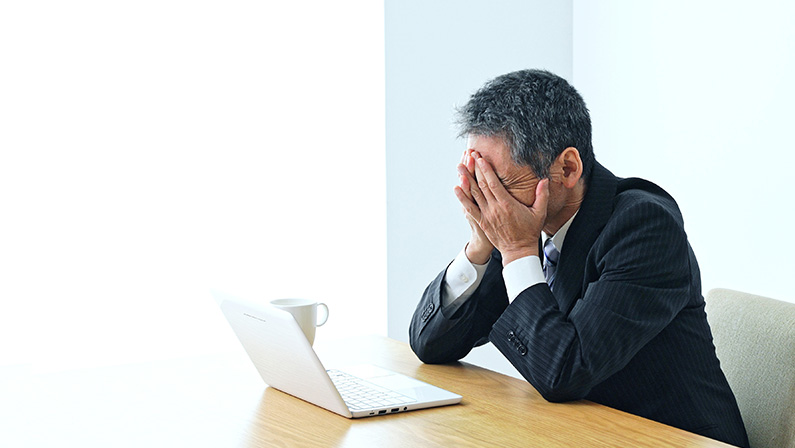 A stressed businessman covers his face at his desk, overwhelmed by challenges caused by labor shortages in the workplace.