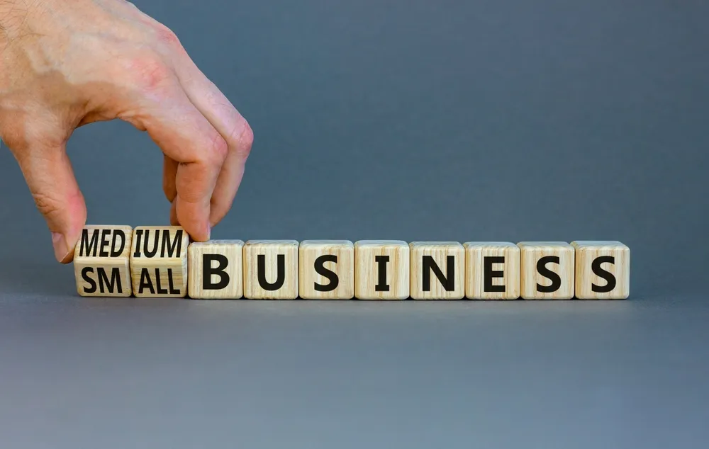Hand arranging wooden blocks to spell small or medium business, symbolizing an SME working with the public sector.